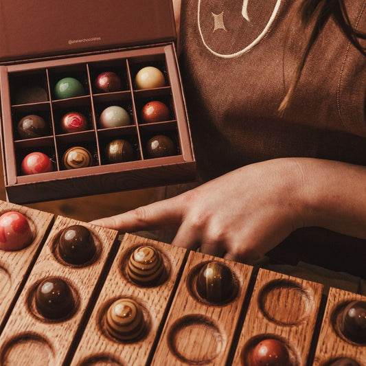 Person holding a box of chocolates with a close-up of a wooden chocolate display. build your own chocolate box.